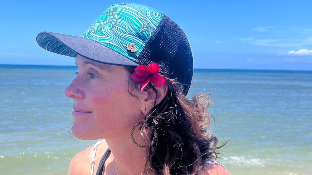 Female model on coast wearing the Waves Trucker Hat, highlighting eco-friendly beach style and breathable design.