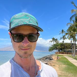 Male model styling the Waves Trucker Hat, featuring ocean print, adjustable mesh back, and casual surf style.